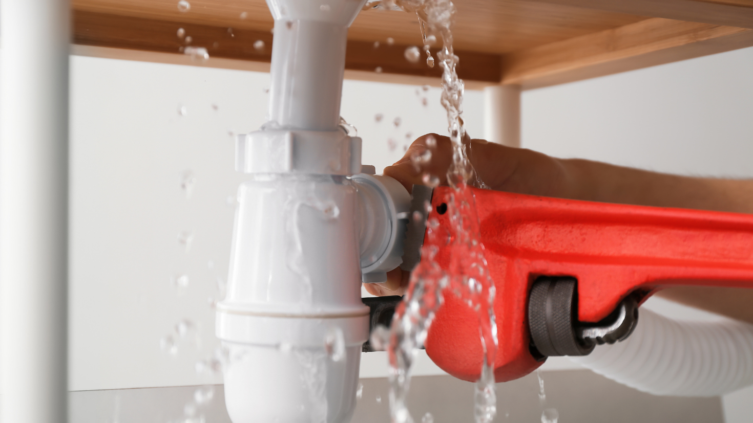 A person is holding a red wrench under a sink